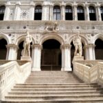 Stone statues on ornate building with grand staircase.